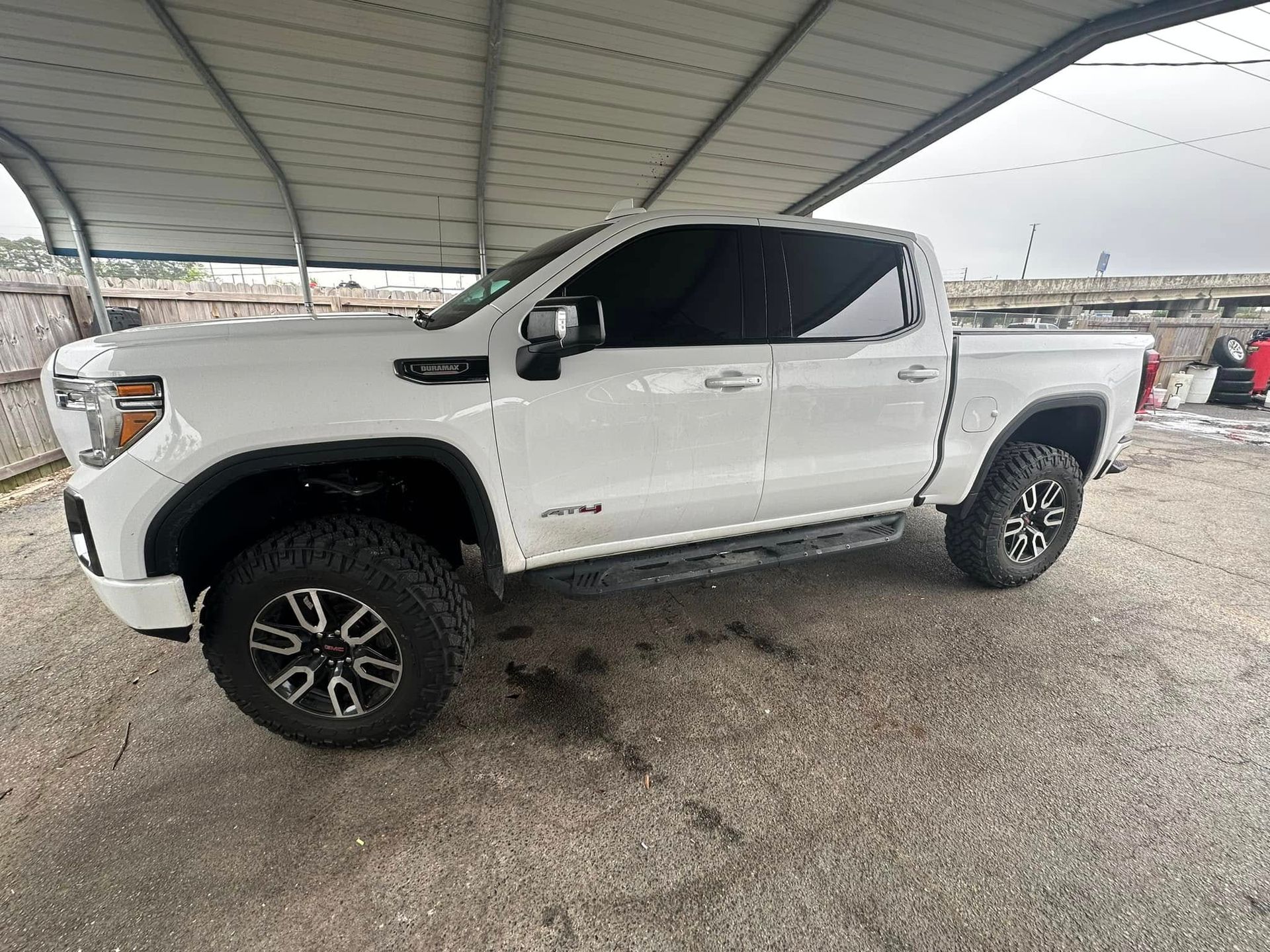 A white truck is parked under a canopy in a parking lot.
