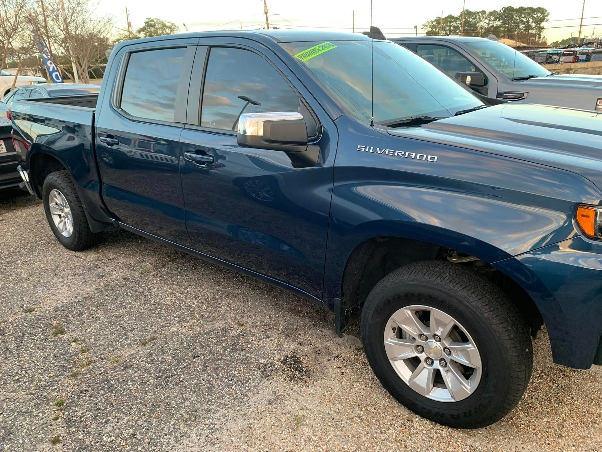 A blue pickup truck is parked in a gravel lot.