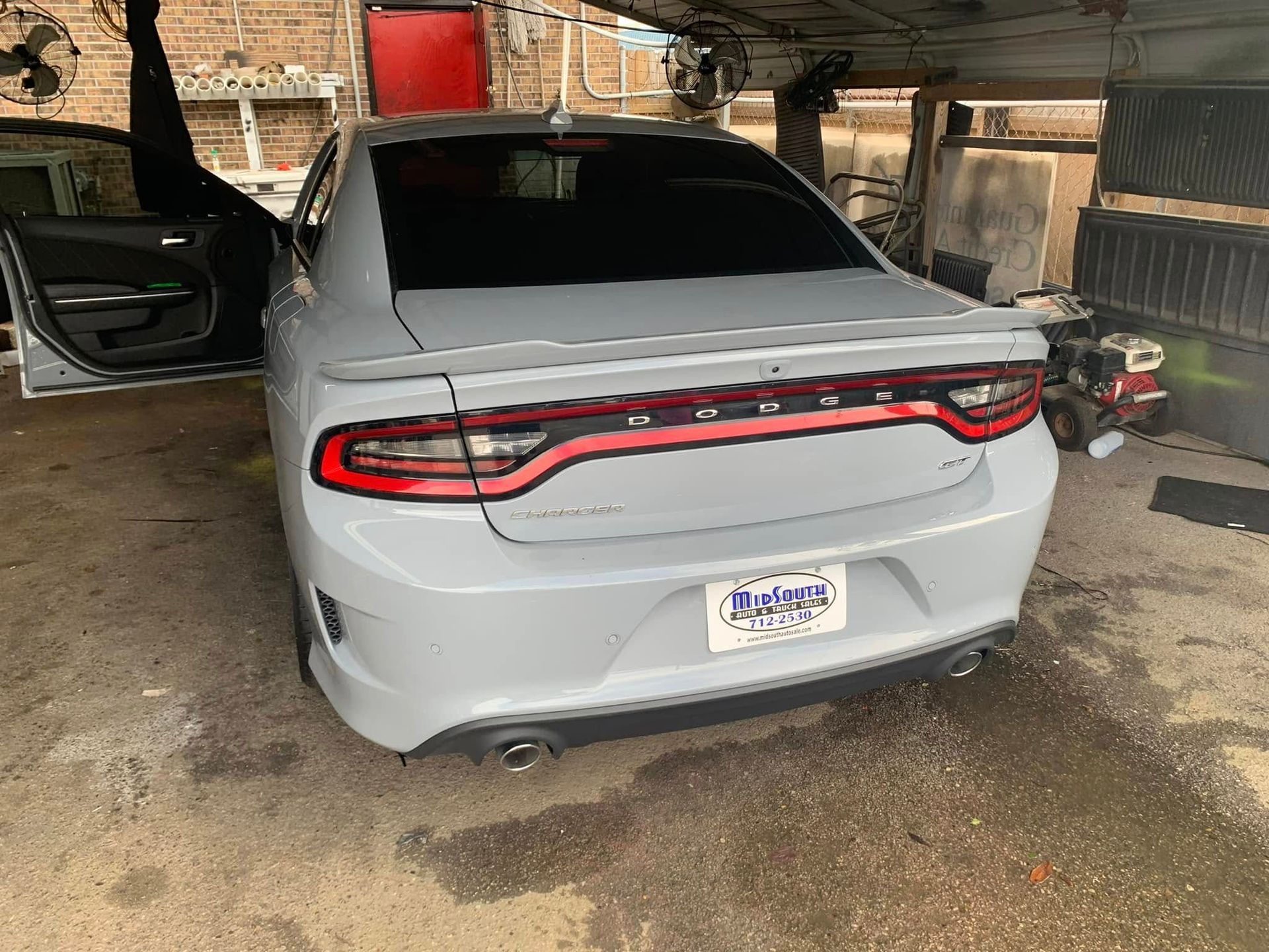 A white dodge charger is parked in a garage with its doors open.
