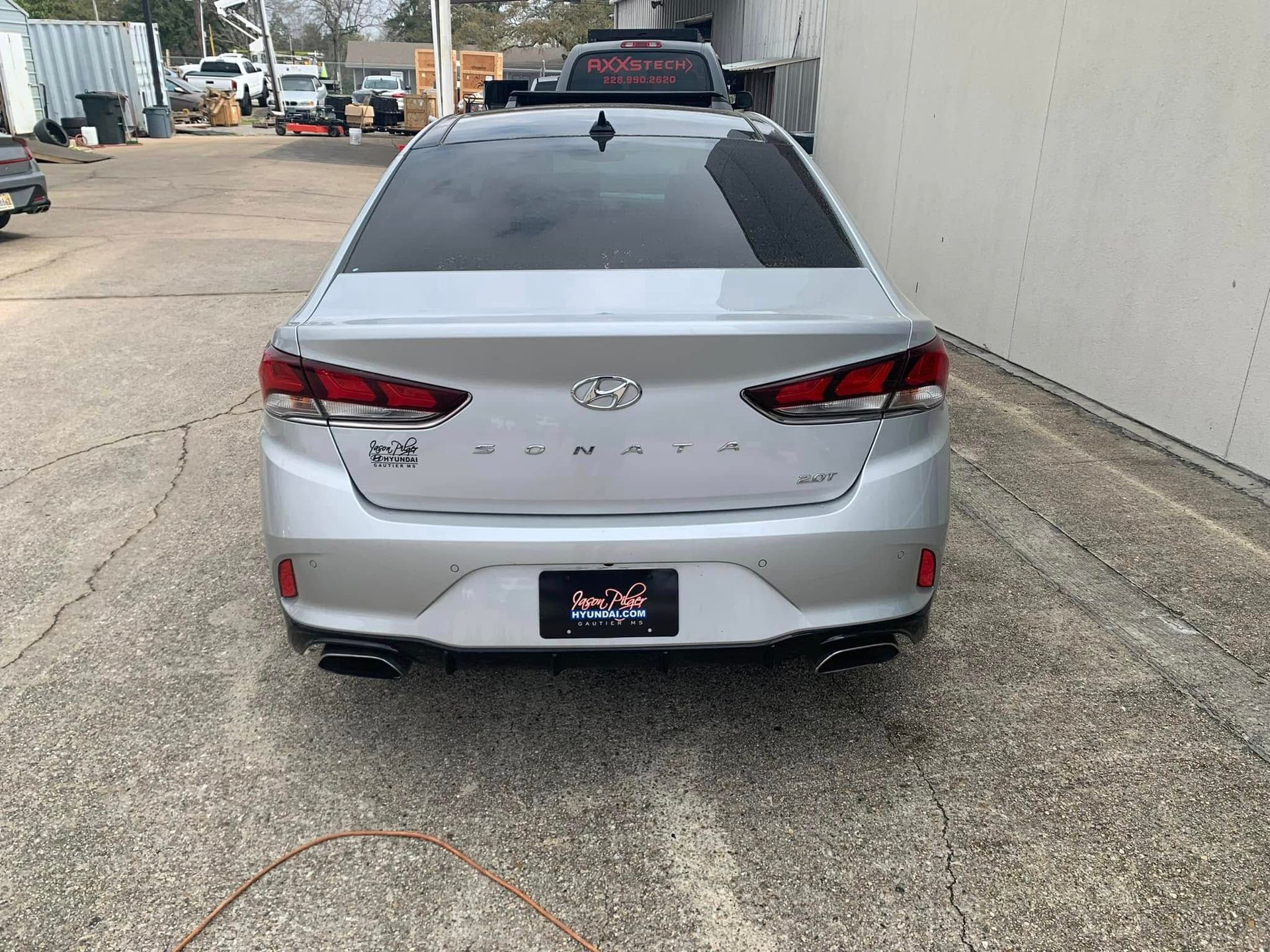 The back of a silver hyundai sonata is parked in a parking lot.