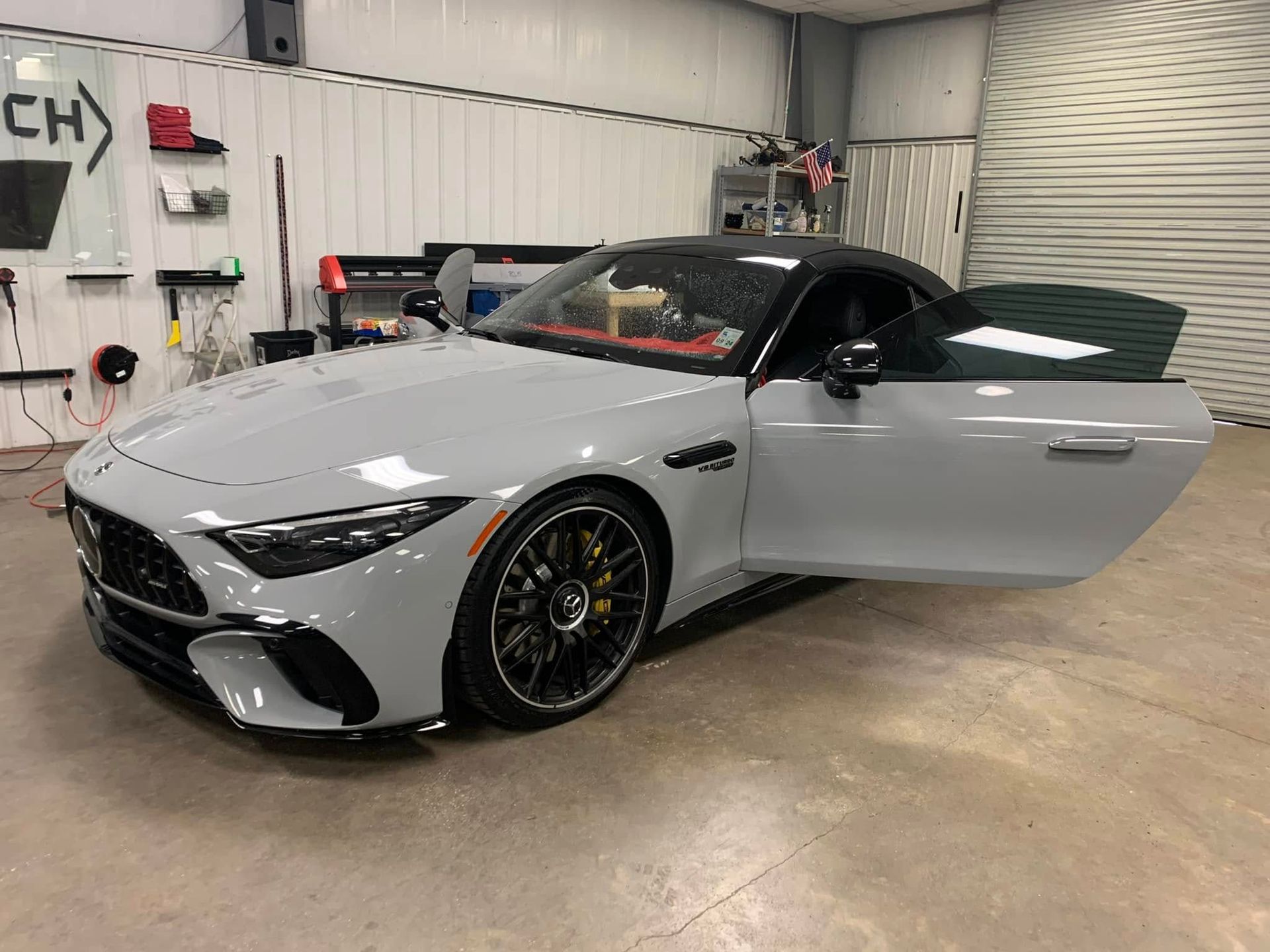 A white sports car is parked in a garage with its doors open.