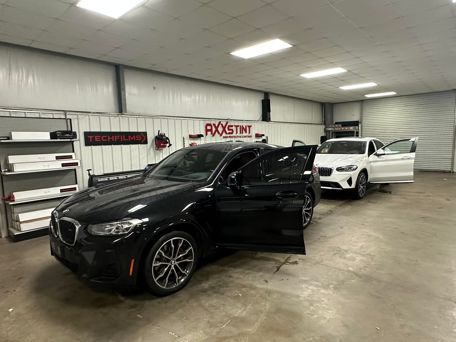 A black car is parked in a garage next to a white car.