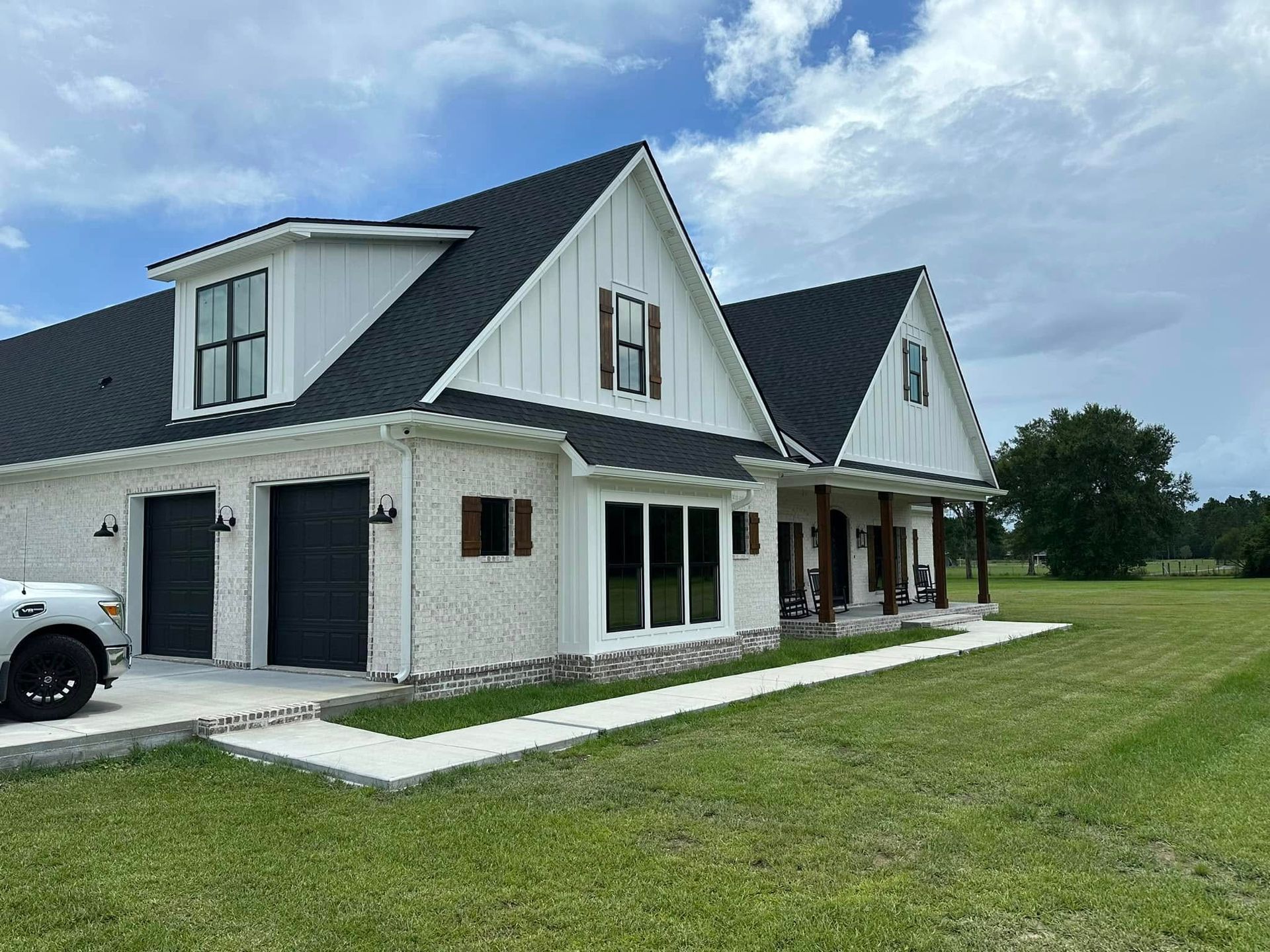A white truck is parked in front of a large white house with a black roof.