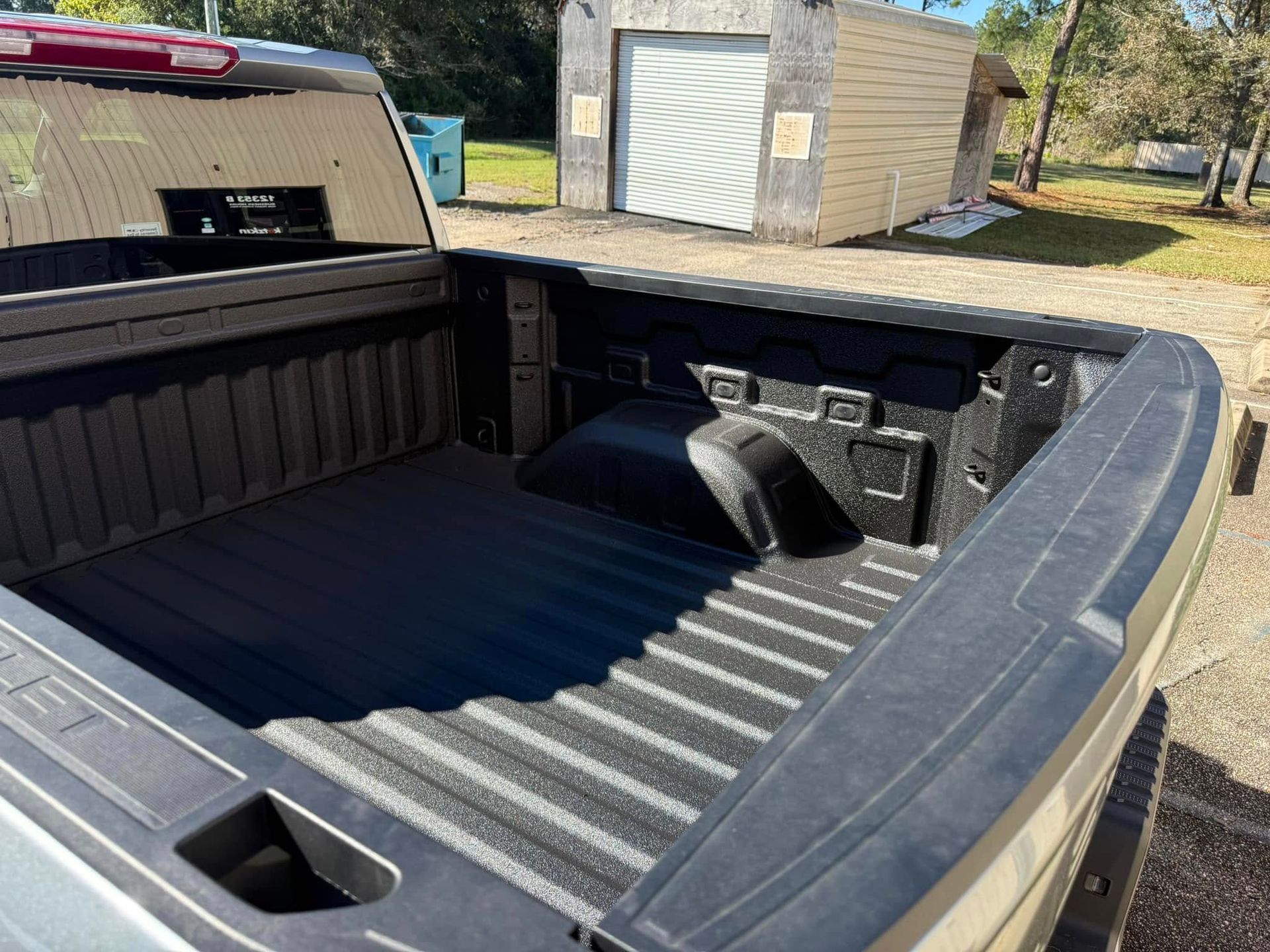 The back of a truck with the bed open and a garage in the background.