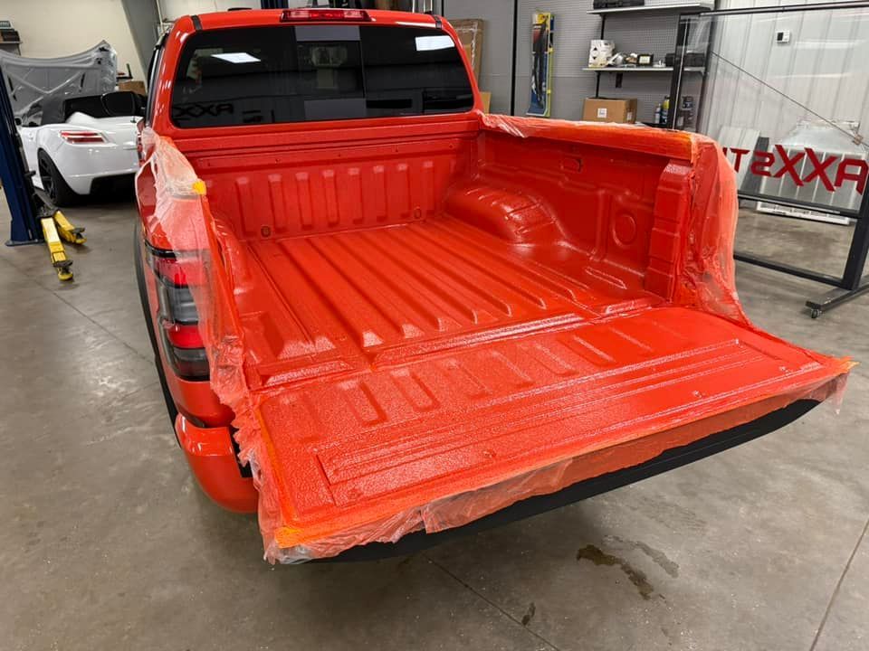 A red truck is being painted in a garage.