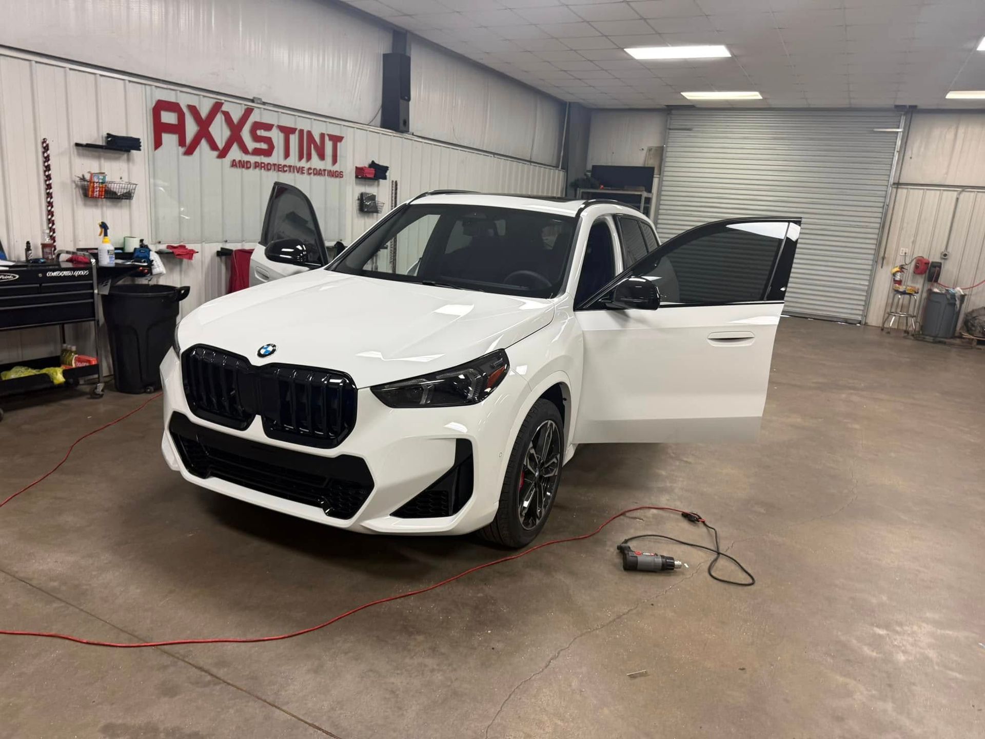 A white bmw x5 is parked in a garage with its doors open.