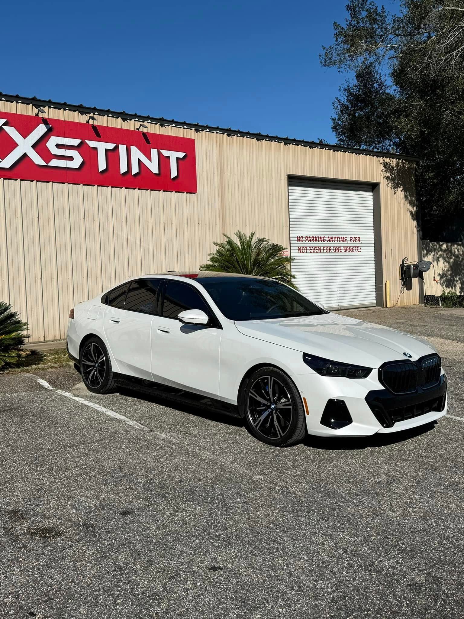 A white car is parked in front of a building that says xstint.