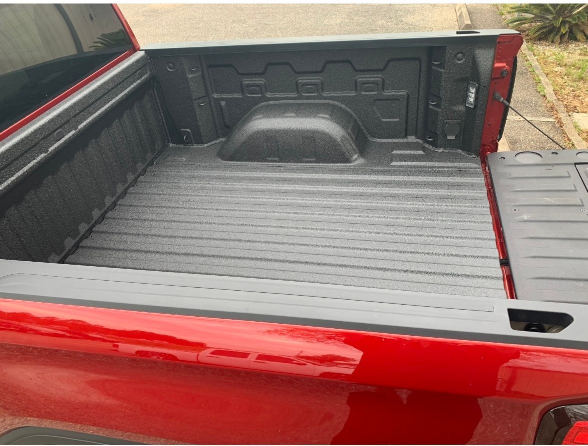 The bed of a red truck is painted black.