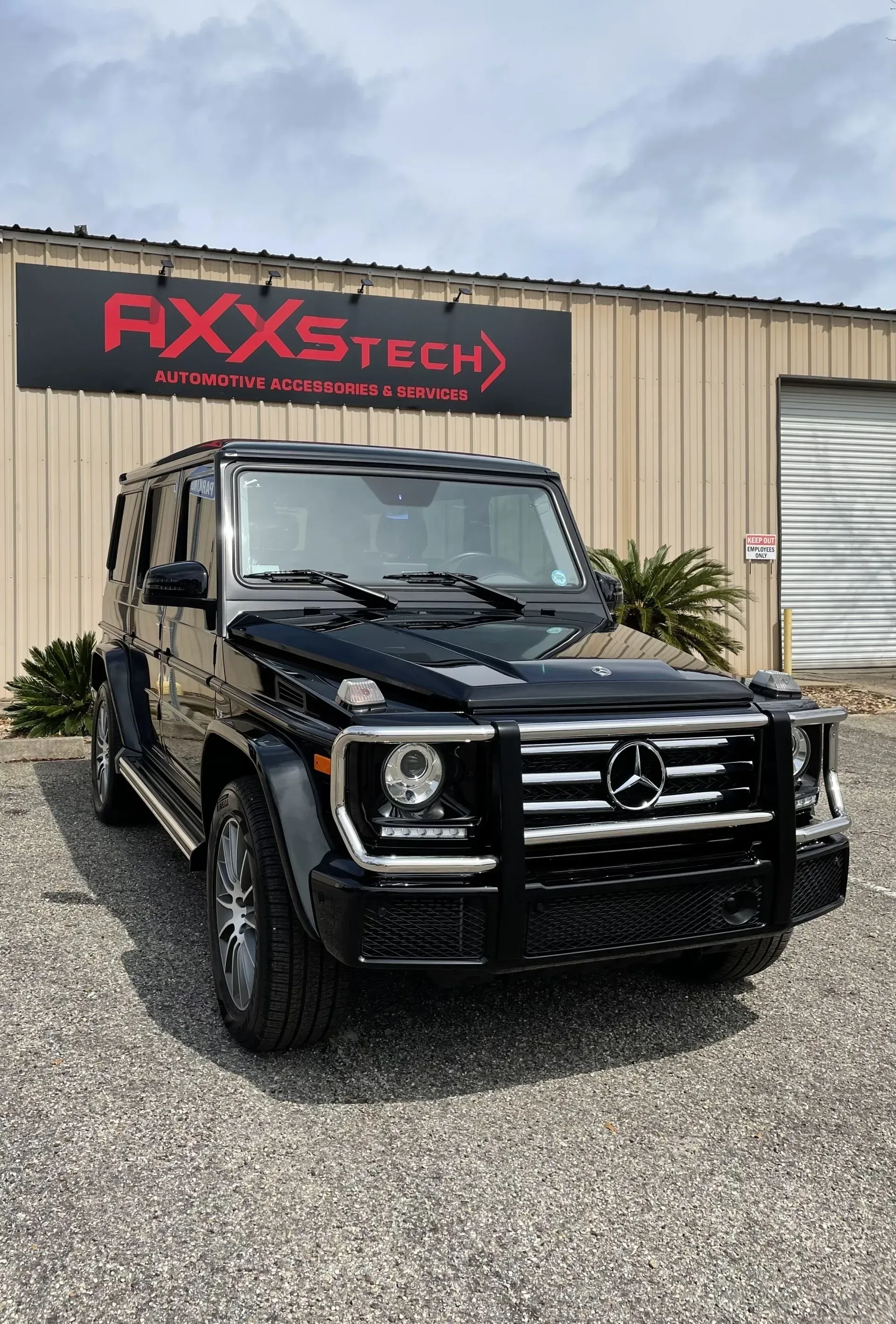 A black mercedes benz g class is parked in front of a building.