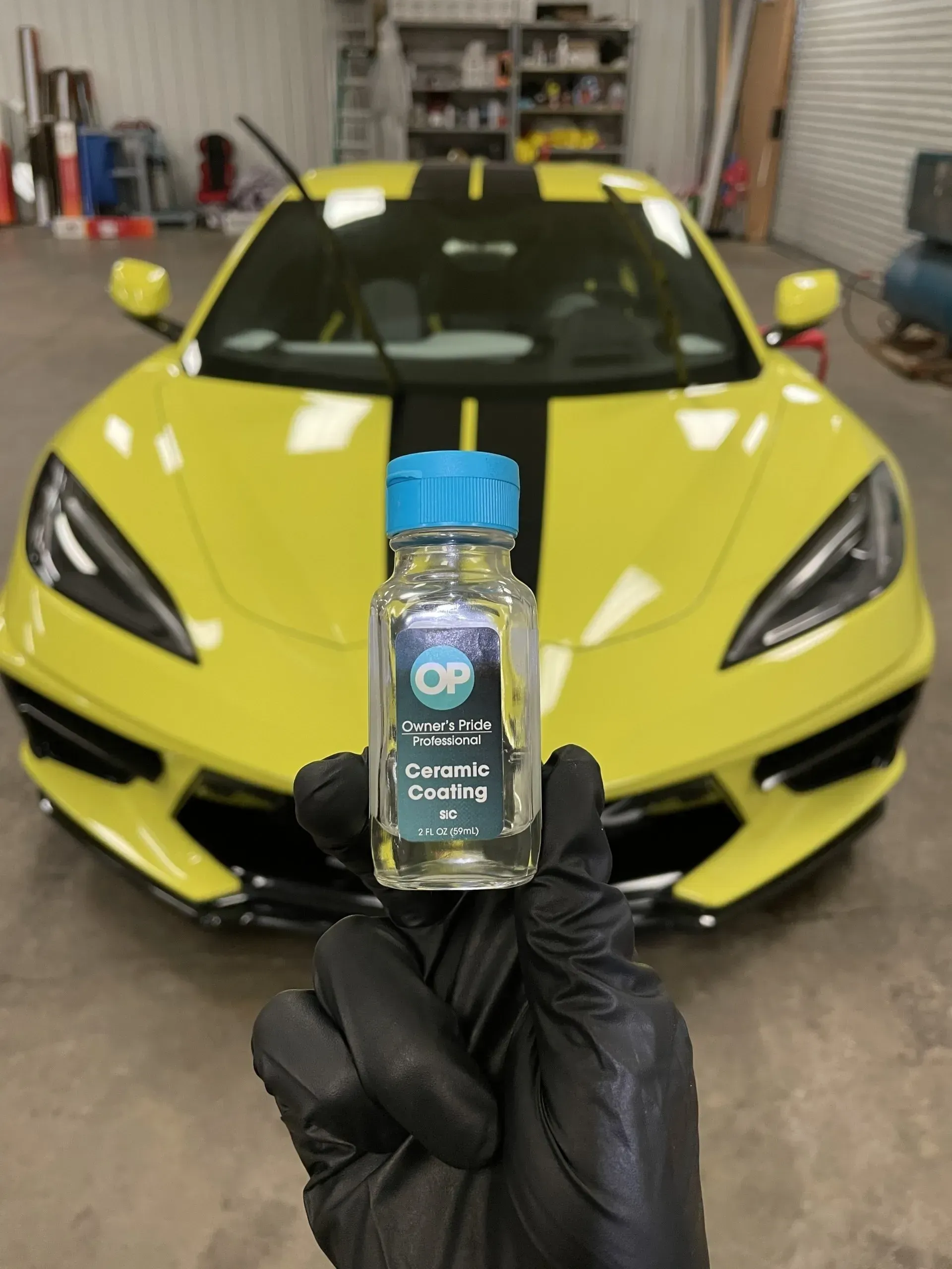 A person holding a bottle of ceramic coating in front of a yellow sports car
