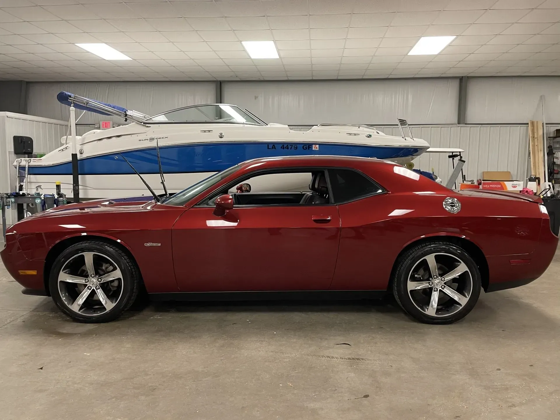 A red dodge challenger is parked in a garage next to a boat.