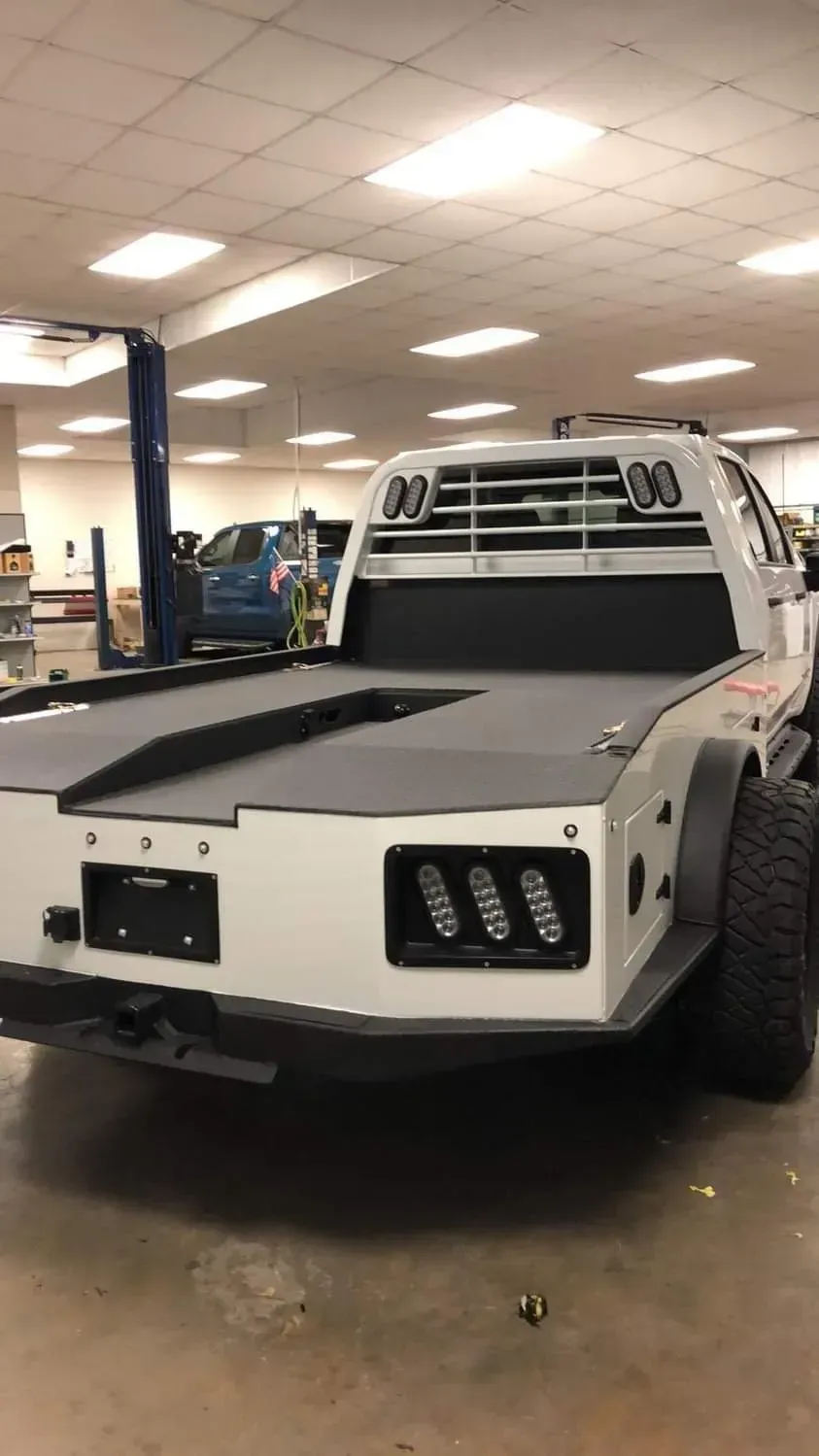 A white truck with a flat bed is parked in a garage.