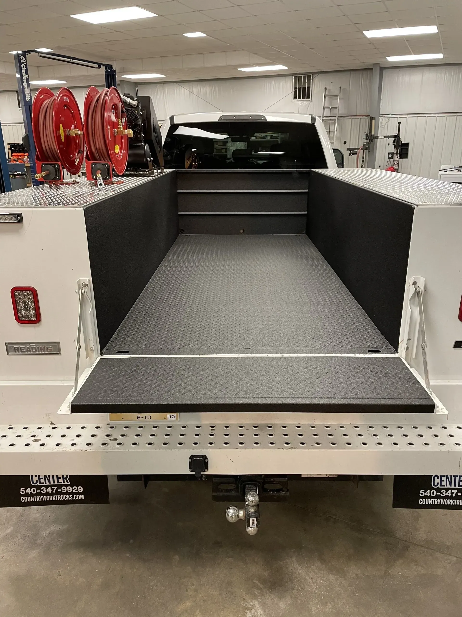 A white truck is parked in a garage with the bed open.