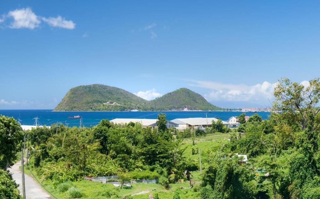 Green hills rise from the sea under a blue sky, with trees and a village in the foreground.