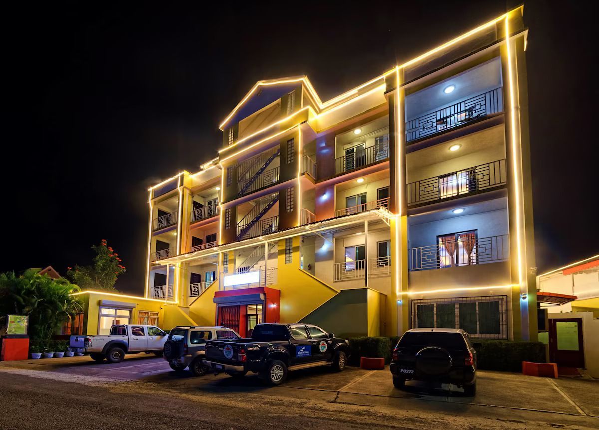 Hotel exterior at night, lit with yellow lights; several vehicles parked in front.