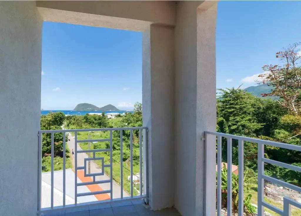 Balcony view of ocean, road, and lush greenery under a clear blue sky.