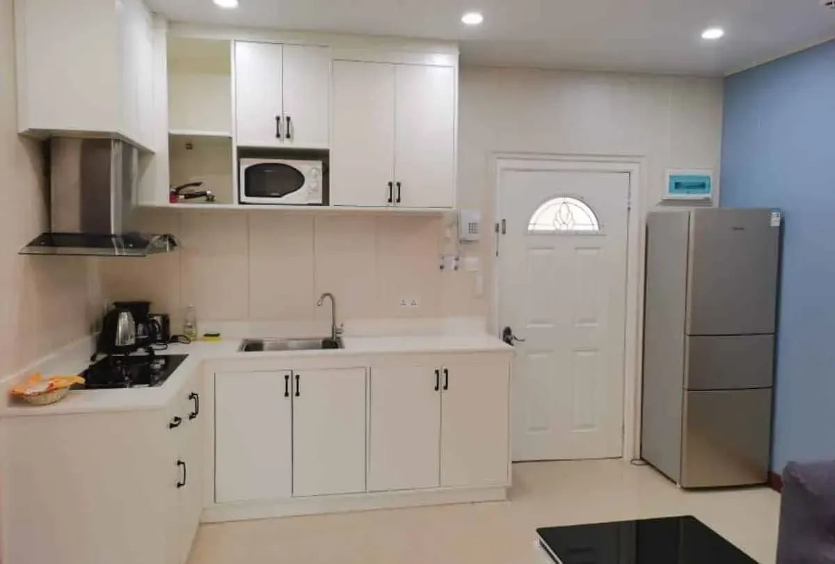 White kitchen with cabinets, microwave, sink, and refrigerator. A door and blue wall are also visible.