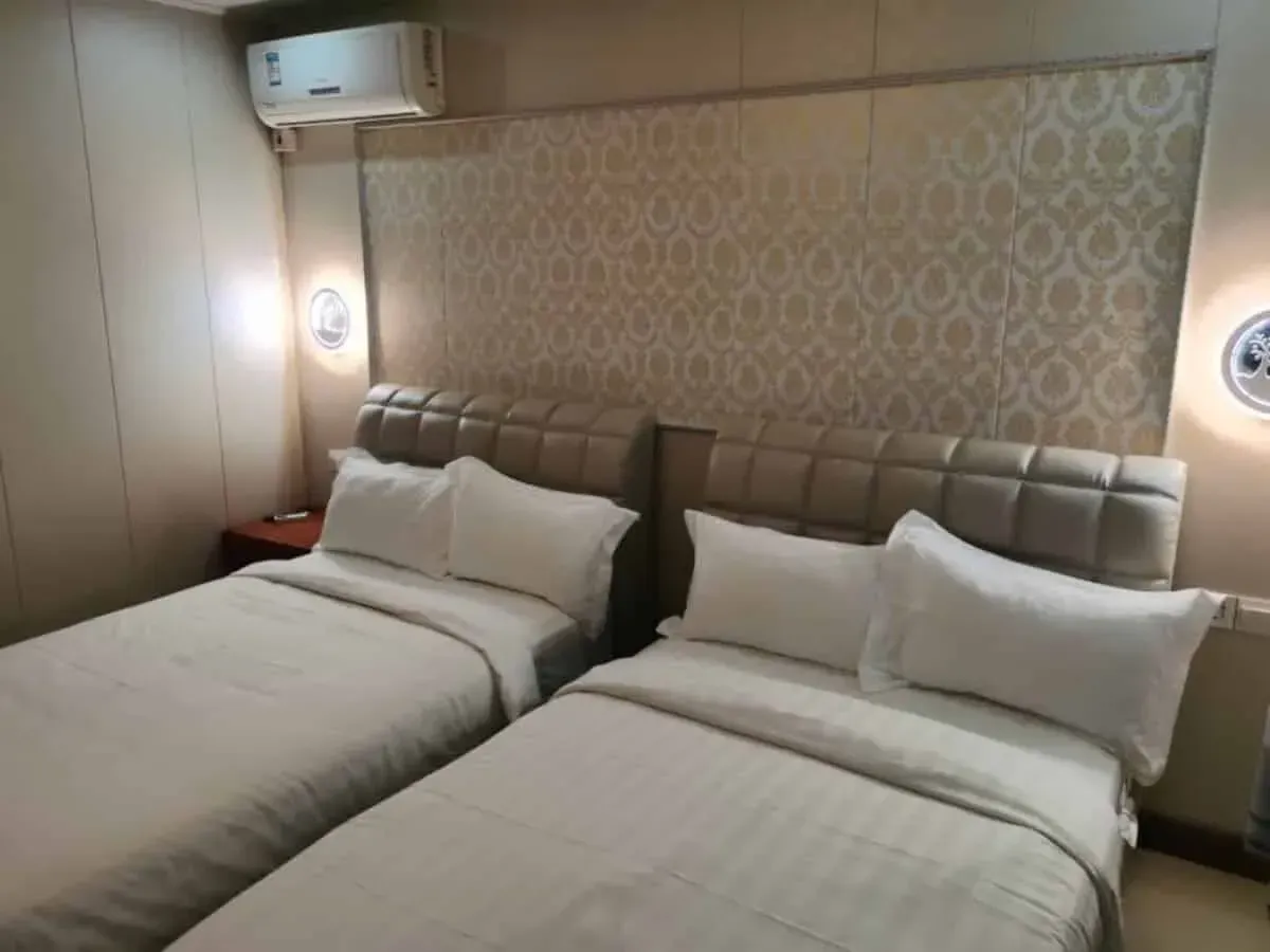 Two twin beds in a hotel room with white bedding. Beige patterned headboard, AC unit.