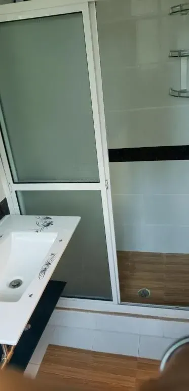 Bathroom with a white sink, glass shower door, and wooden floor.