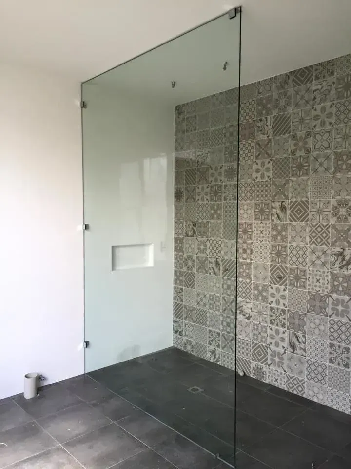 Walk-in shower with frameless glass, grey tiles, patterned feature wall, and built-in wall shelf.