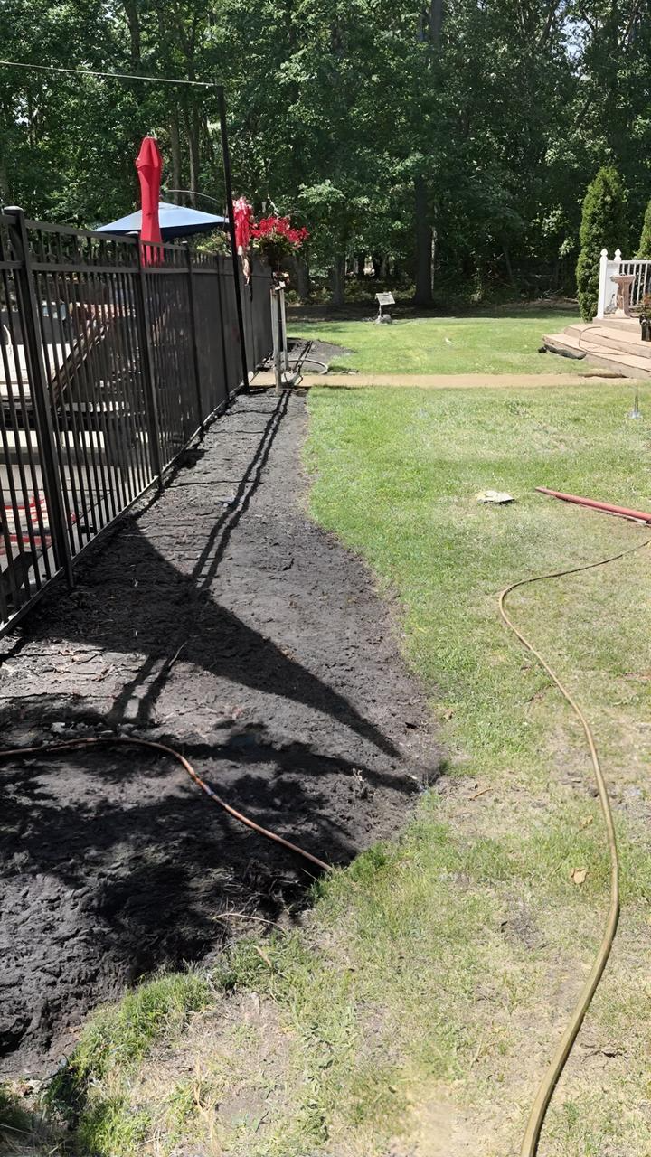 Black metal fence beside a grassy yard and mulch path, with red ribbons and trees in the background