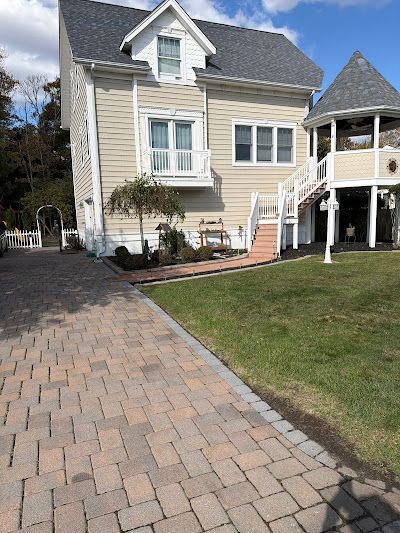 Light yellow house with a brick driveway, a side turret, and a white staircase leading to an elevated deck