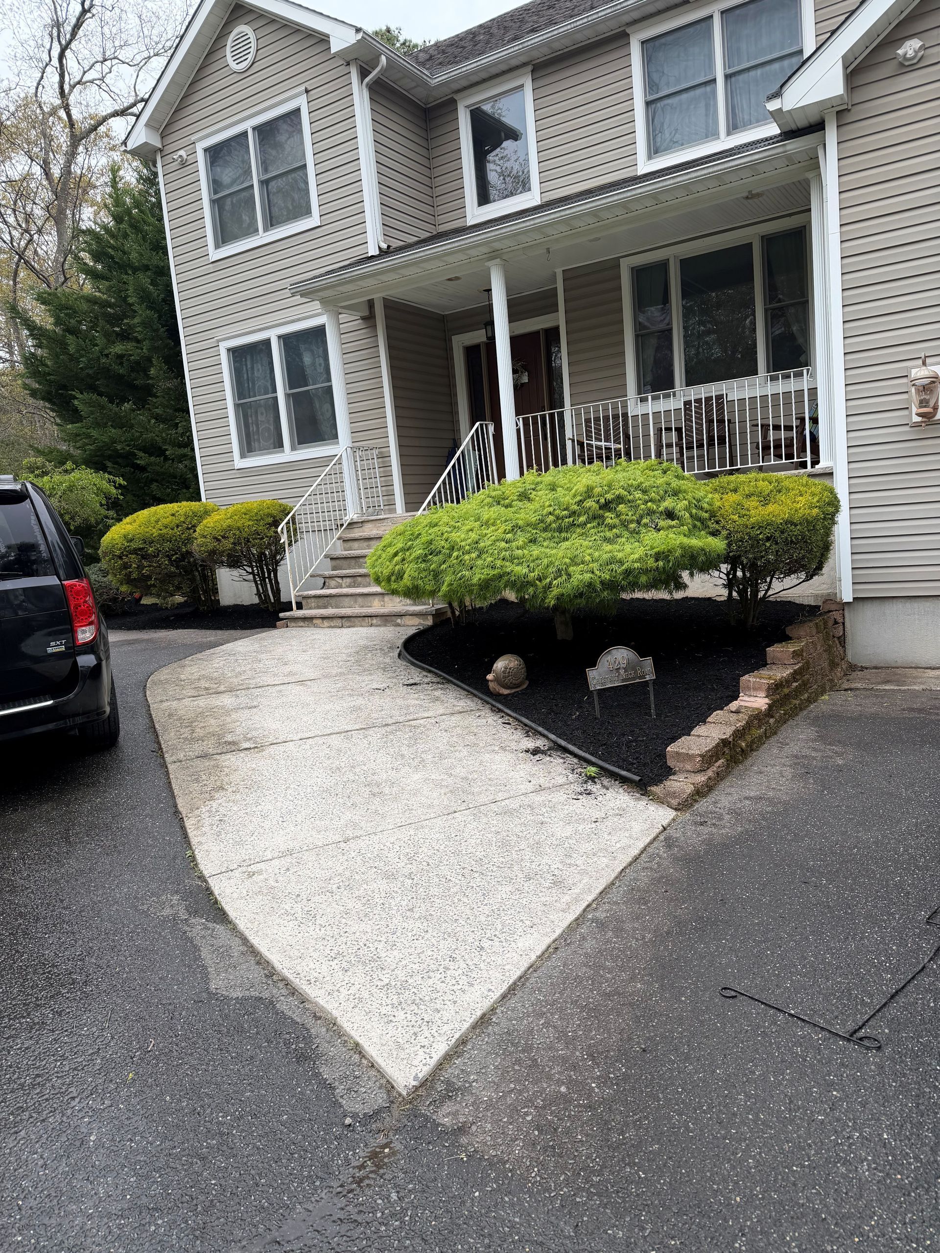 Suburban townhouse exterior with white front porch, shrubs, and a wet driveway on a cloudy day