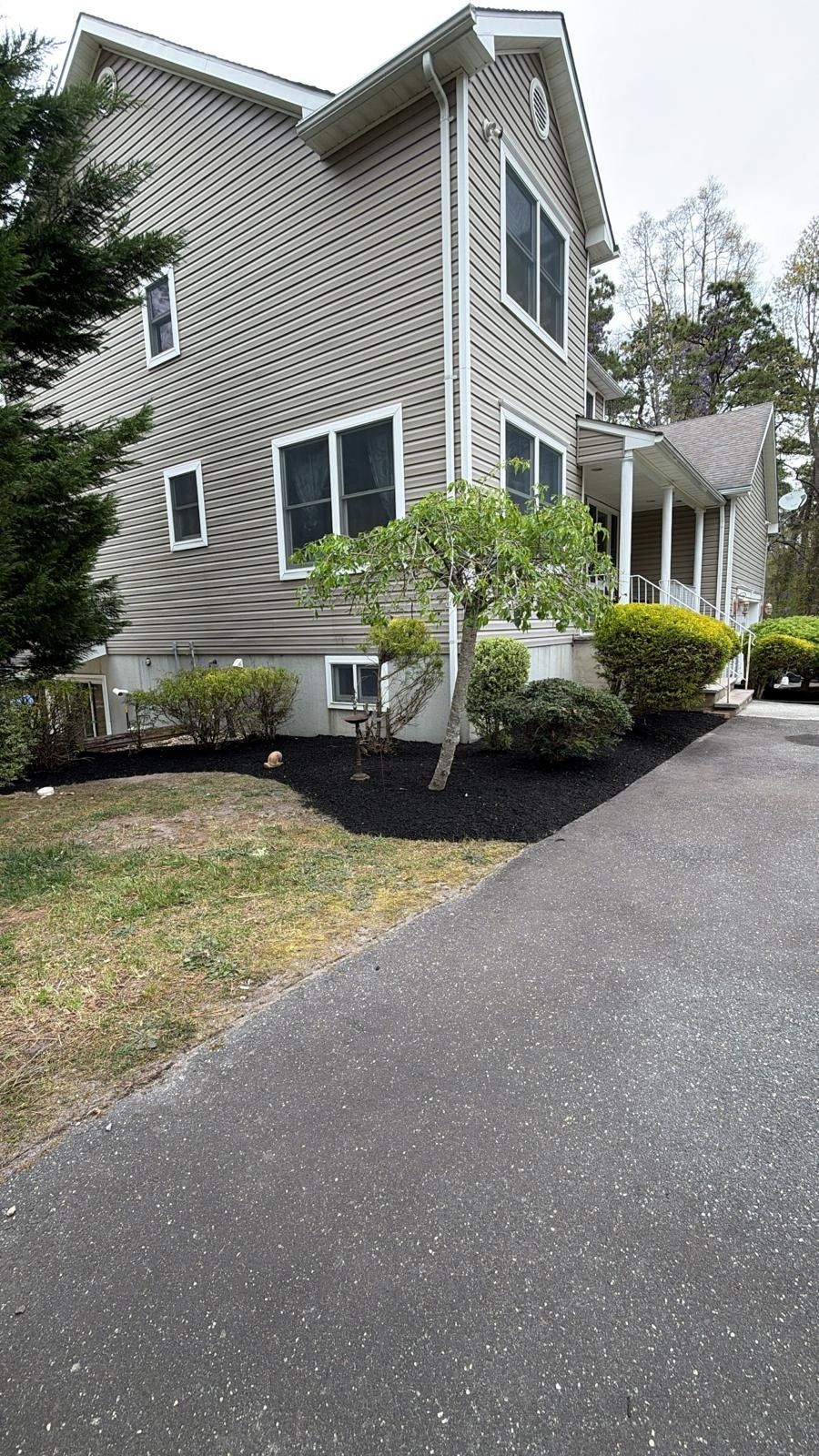 Two-story gray house with white trim, dark roof, and landscaped front yard beside a paved driveway