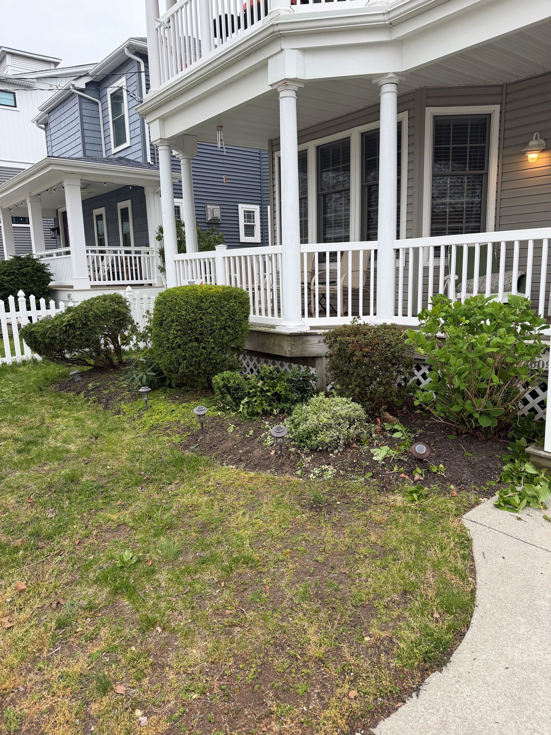 Porch with white railing and steps beside a small front yard and sidewalk, next to blue and gray houses