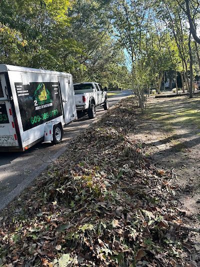 A two brothers and a mower pickup truck with a large trailer parked on the street next to a pile of fallen leaves