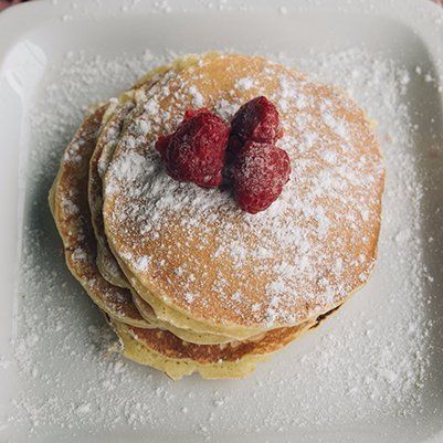 A stack of pancakes with raspberries and powdered sugar on a white plate.