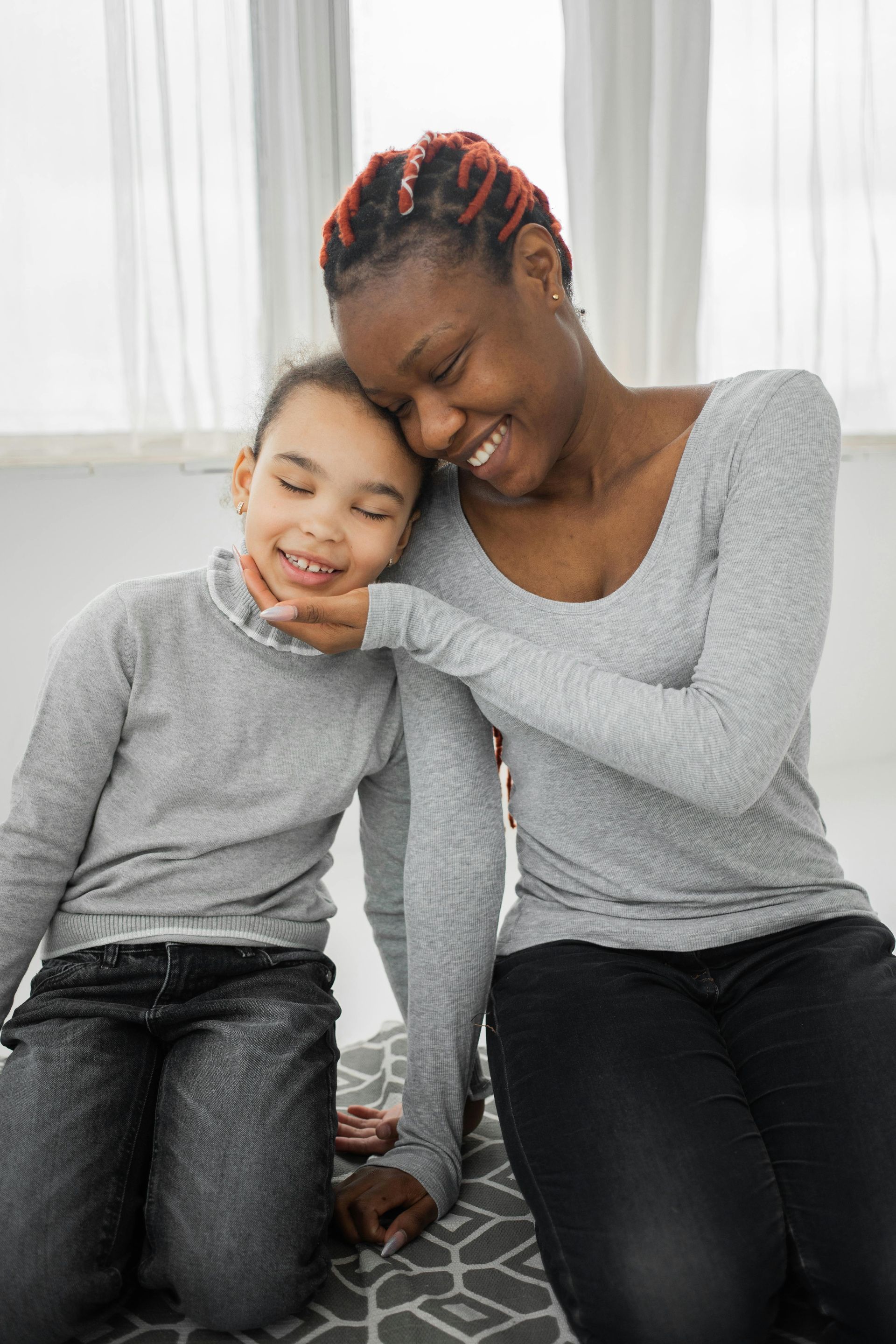 Two people sitting together and smiling, resting heads affectionately in a bright room.