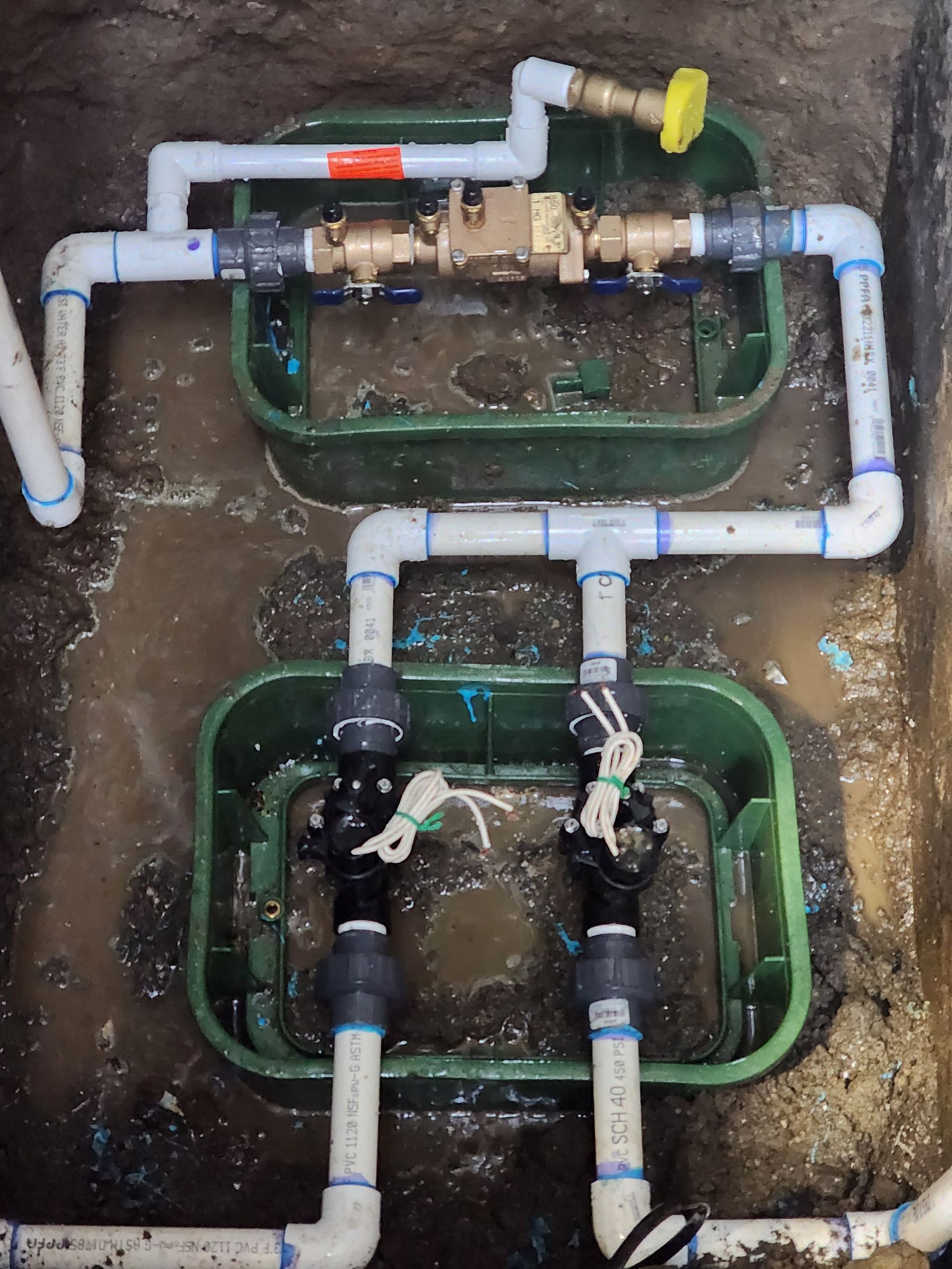 Irrigation system in a green box with pipes, valves, and water meter in the ground.