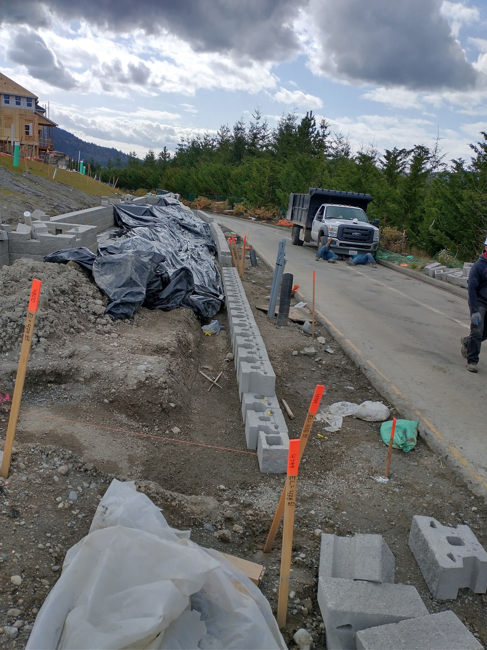 Construction site: cinder block retaining wall under construction next to a road, overcast sky.