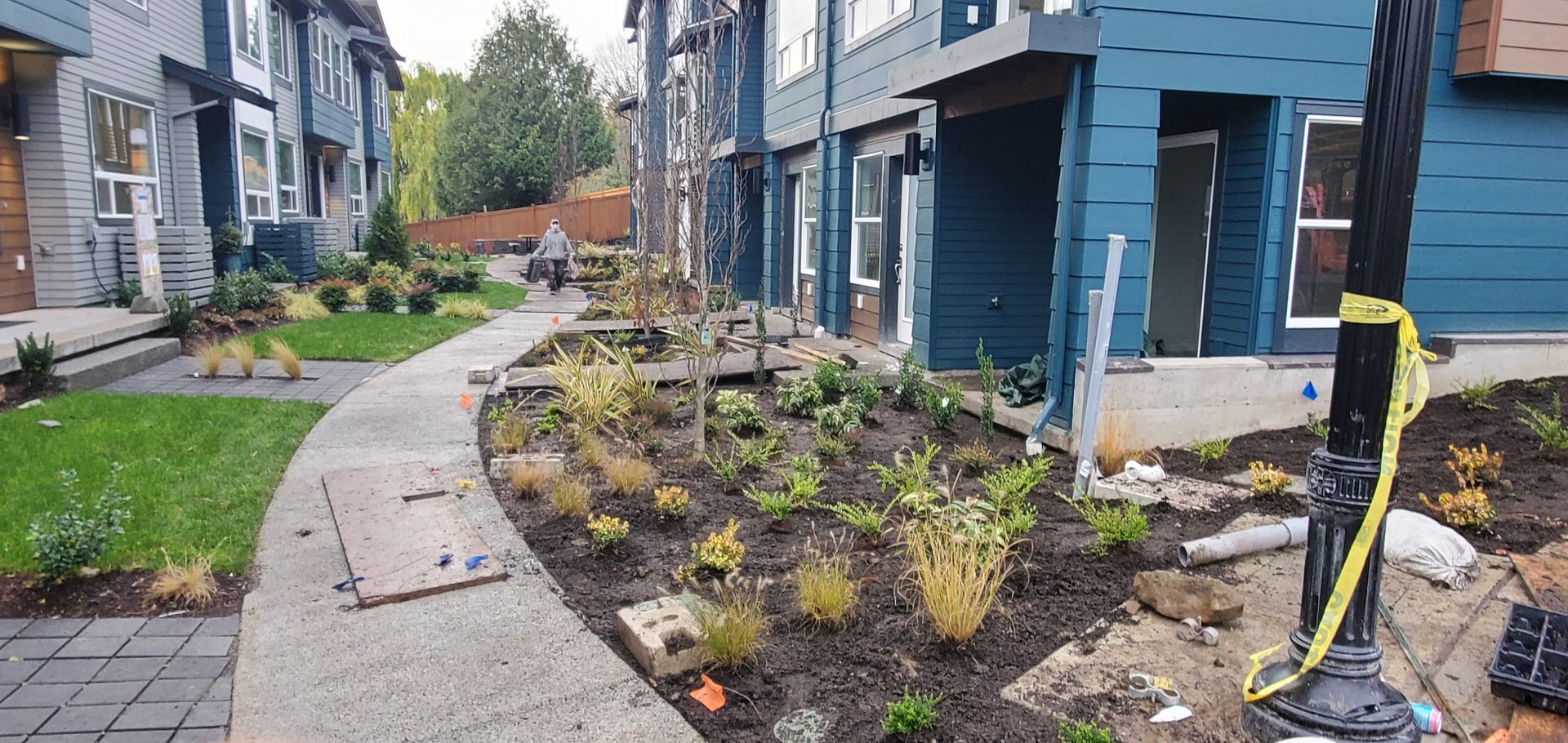 Sidewalk lined with landscaping and blue buildings. Construction materials are visible.
