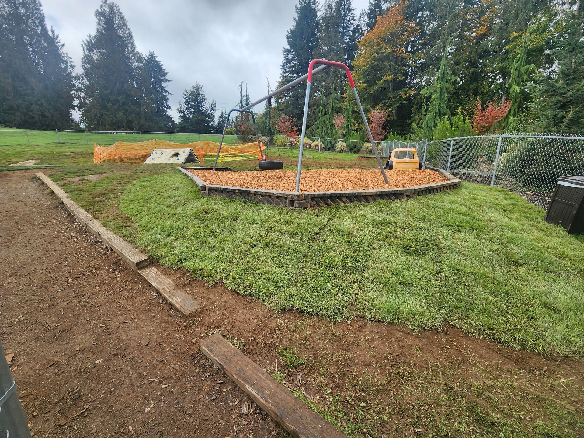 Playground with swings, mulch, grass, and a small toy tractor.