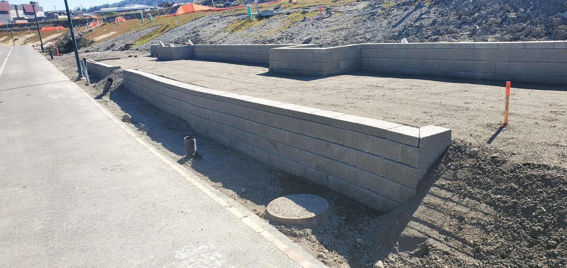 Construction site with concrete retaining walls and a gravel base, next to a paved road.