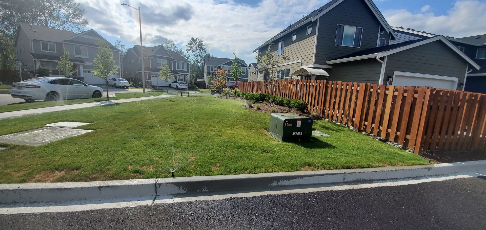 A residential street scene with houses, a fence, and green grass on a sunny day.
