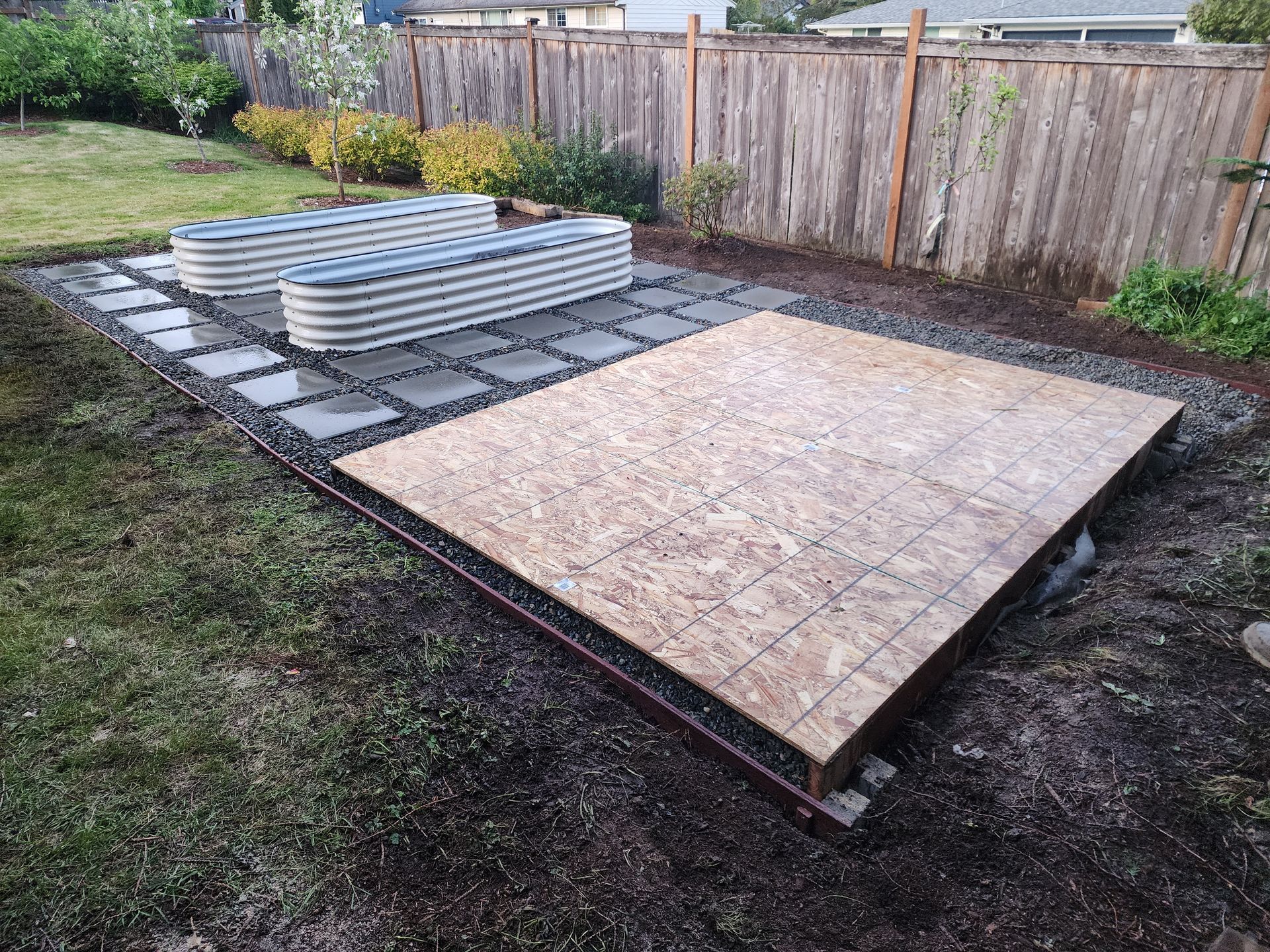 Raised garden beds with pavers and wood platform in a backyard setting.