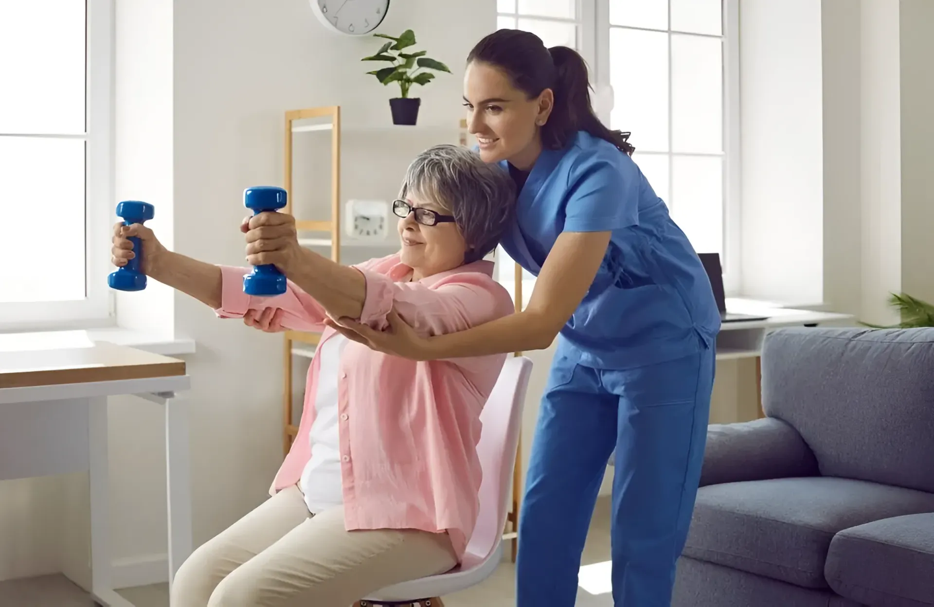 Woman in Scrubs Assists a Seated Person Lifting Weights — Barolin Physiotherapy Services in Bundaberg South, QLD