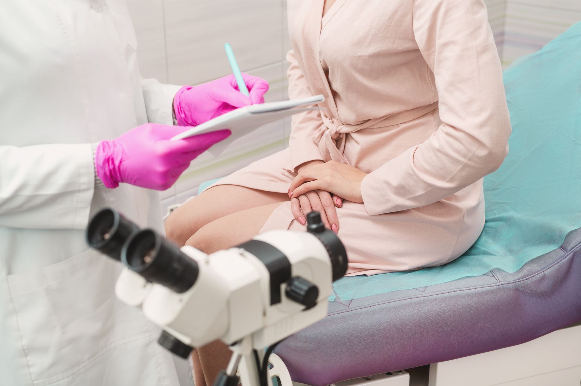 Doctor with pink gloves and clipboard examines patient seated on examination table with colposcope — Barolin Physiotherapy Services in Bundaberg South, QLD
