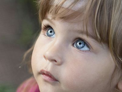 Close-up of a child with blue eyes looking upwards, soft skin, and blonde hair.