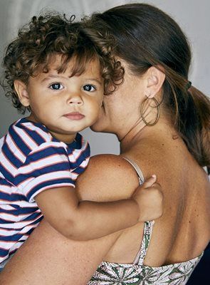 Boy with curly hair held by a woman wearing hoop earrings. Boy is looking forward.