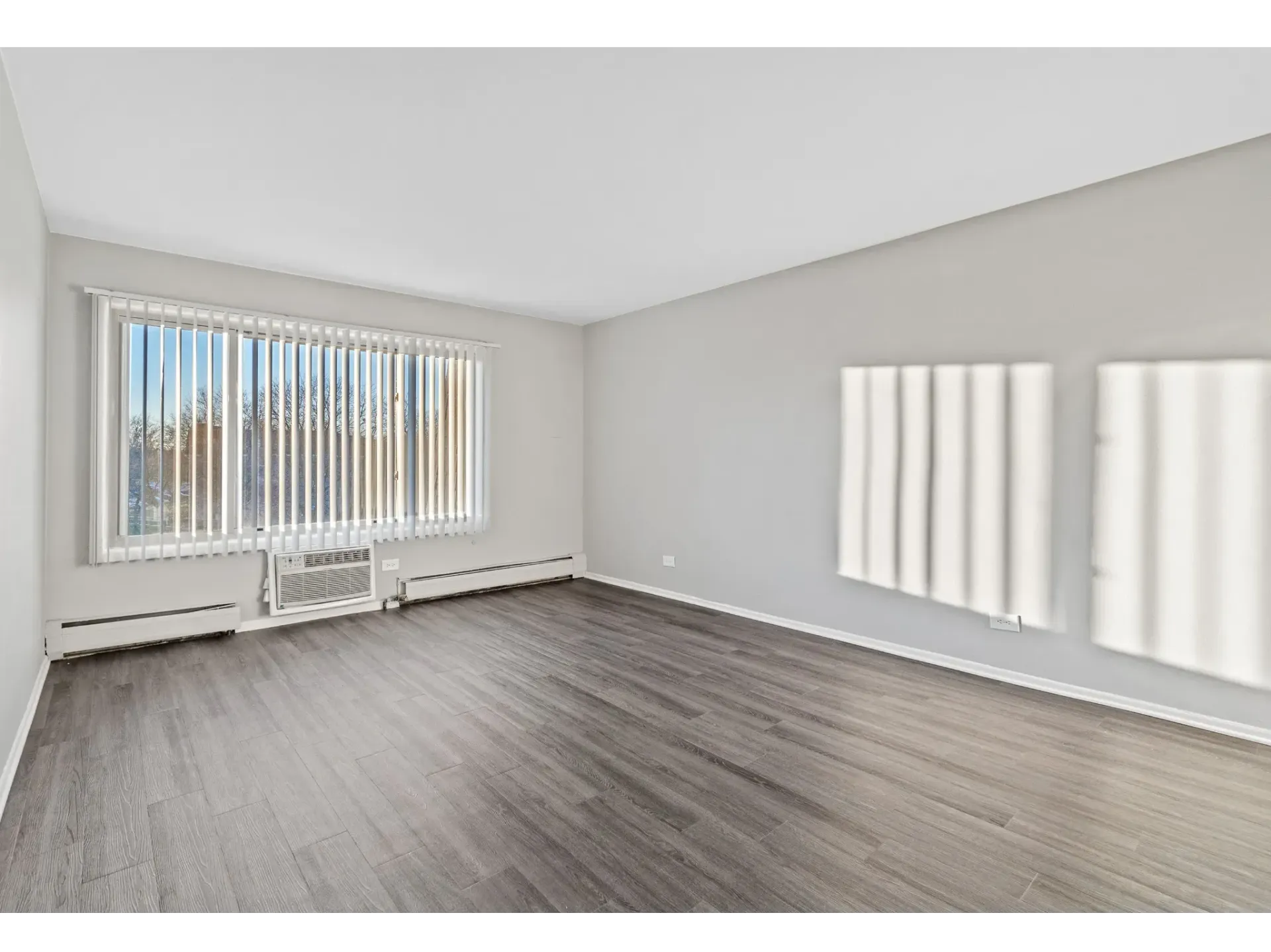 Spacious living room with large window and blinds at Bartlett Lakes, offer apartments for rent in West Chicago, IL.