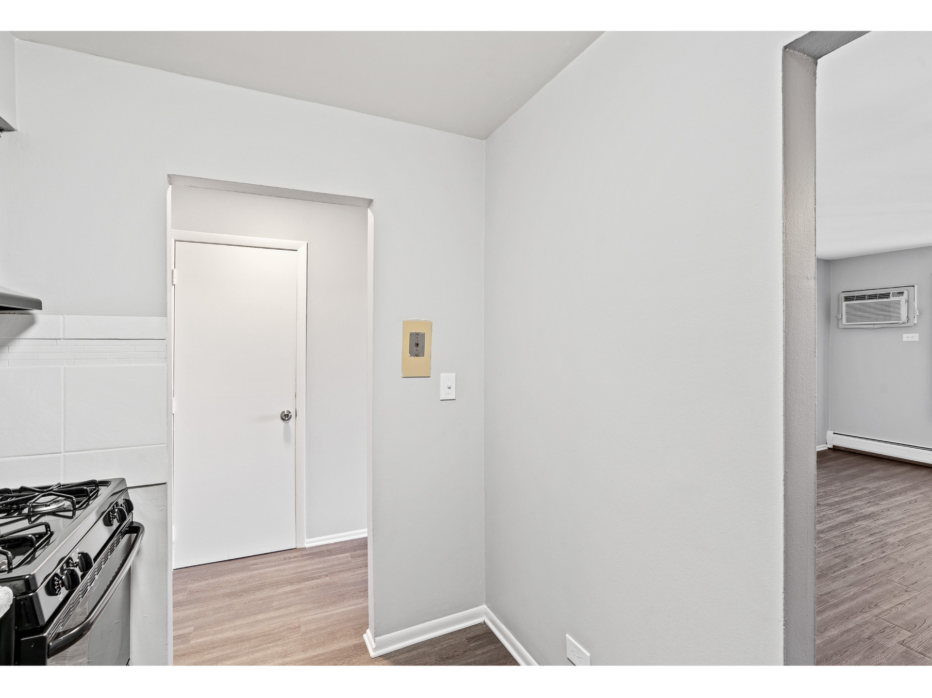 Kitchen area with stove on the left and doorway to a living area with an AC unit on the far wall.