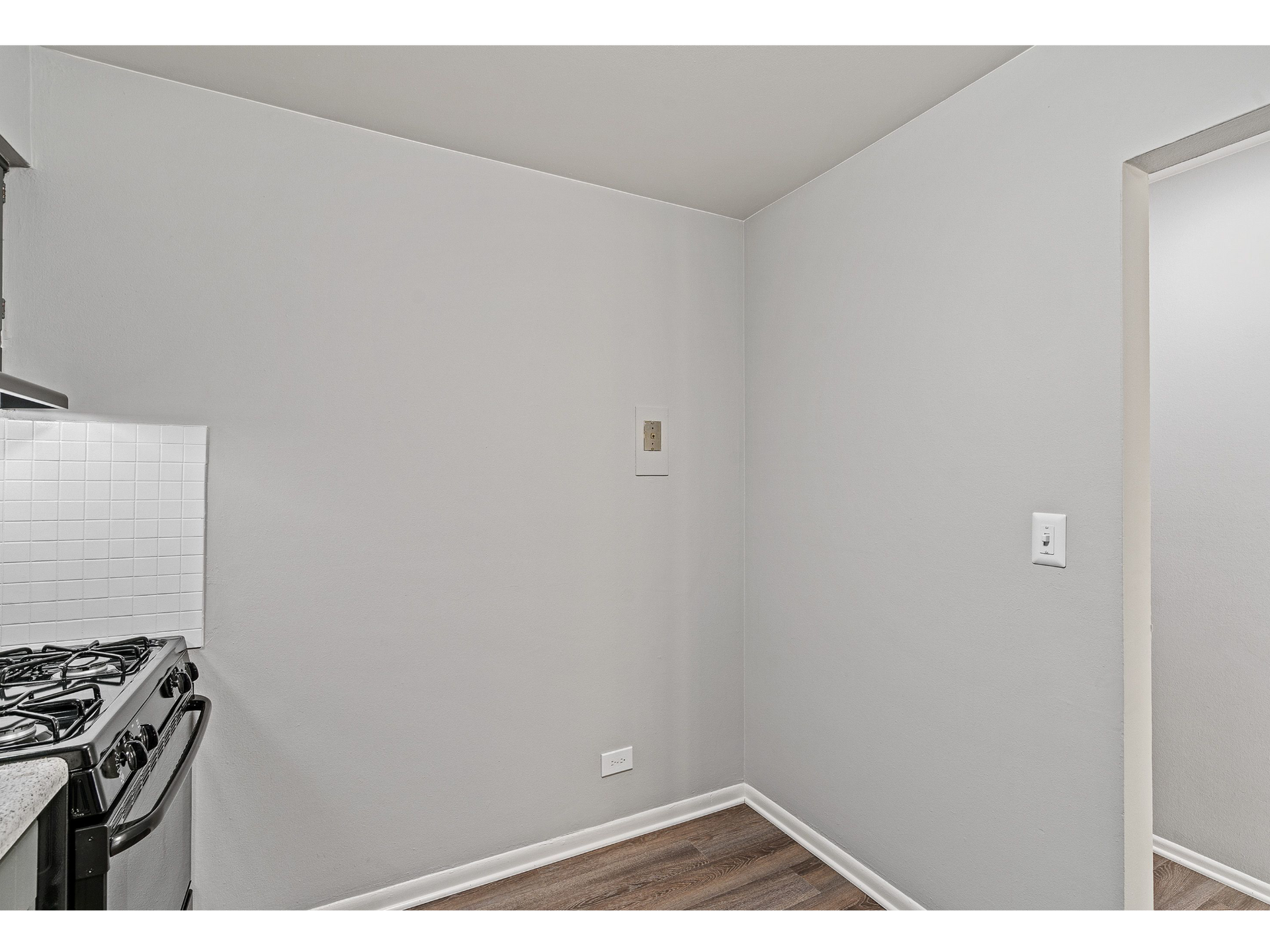 Corner of a small kitchen with a gas stove, gray walls, and wood-look flooring.