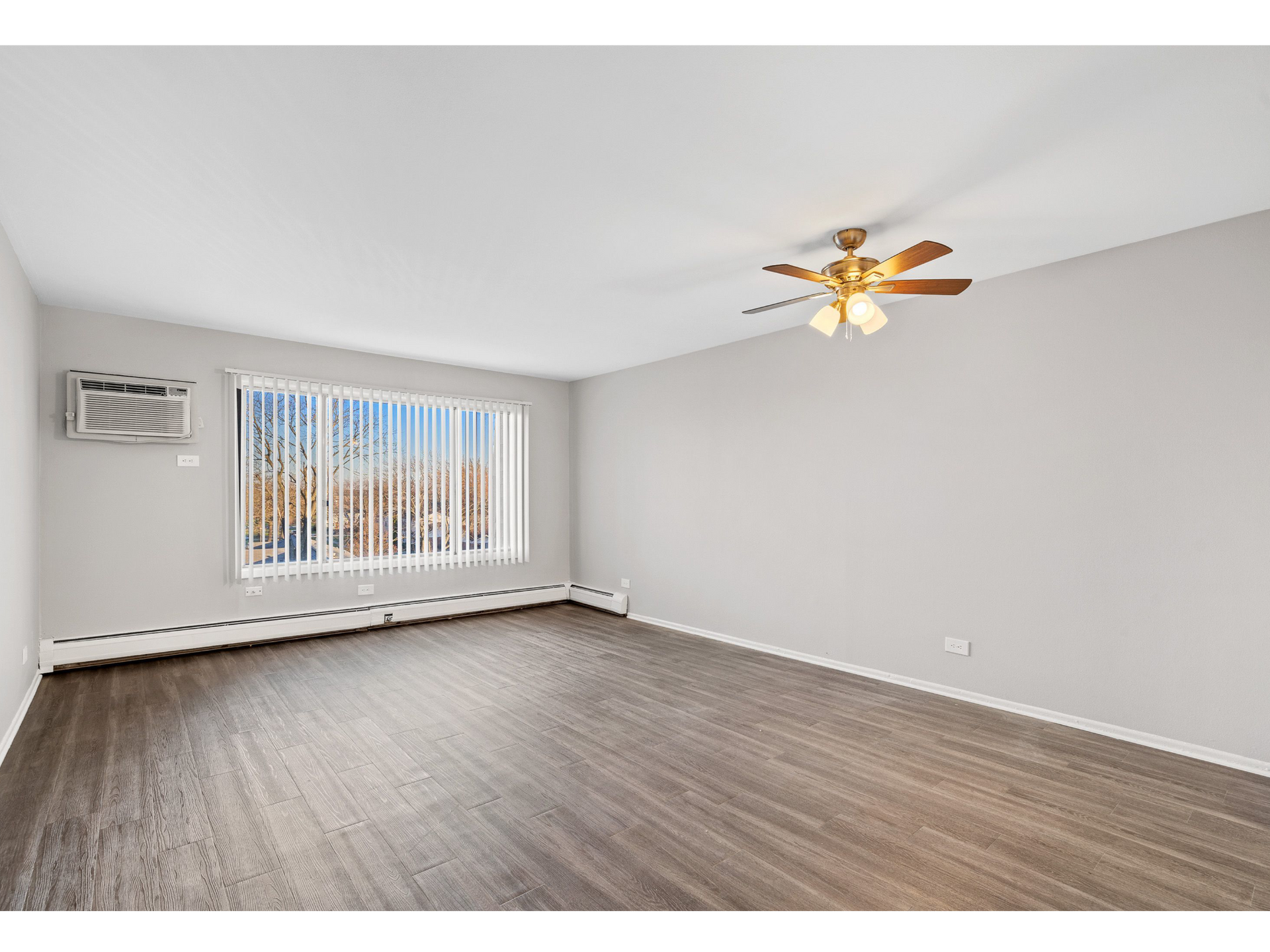 Living room in an apartment with a large window, vertical blinds, and a ceiling fan.