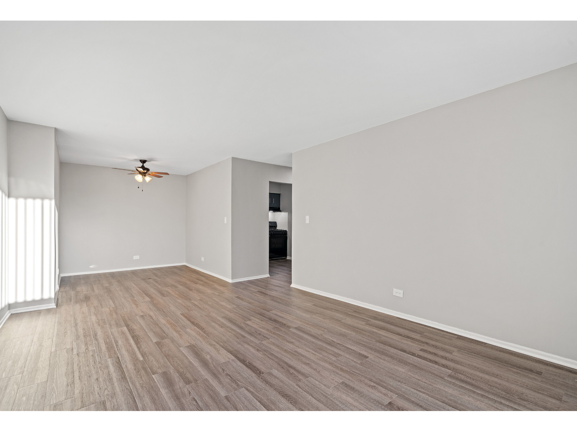 Living room with gray walls, wood-look flooring, ceiling fan, and large window.