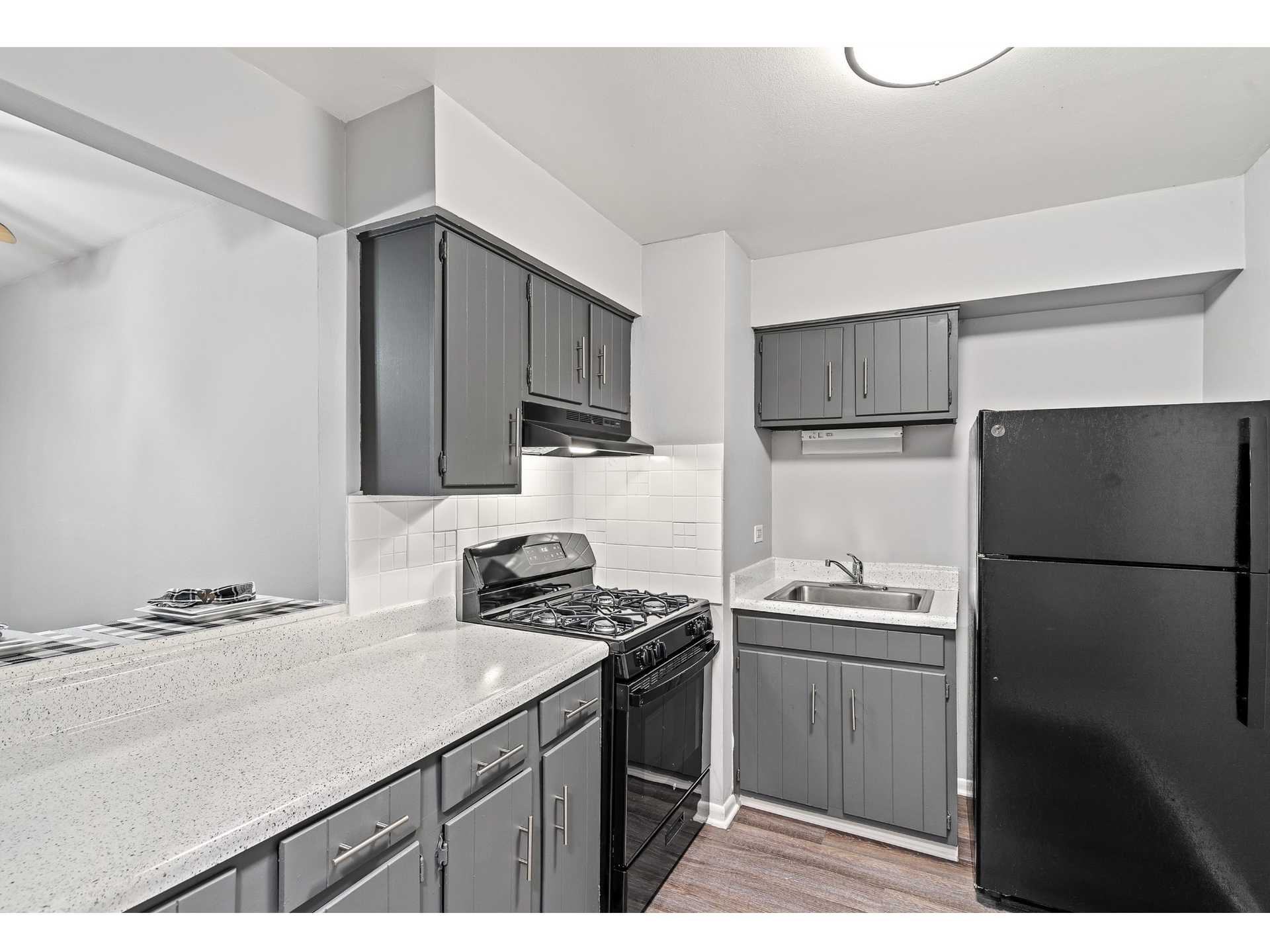 Galley-style kitchen with gray cabinets, white countertops, a sink, stove, and black refrigerator.