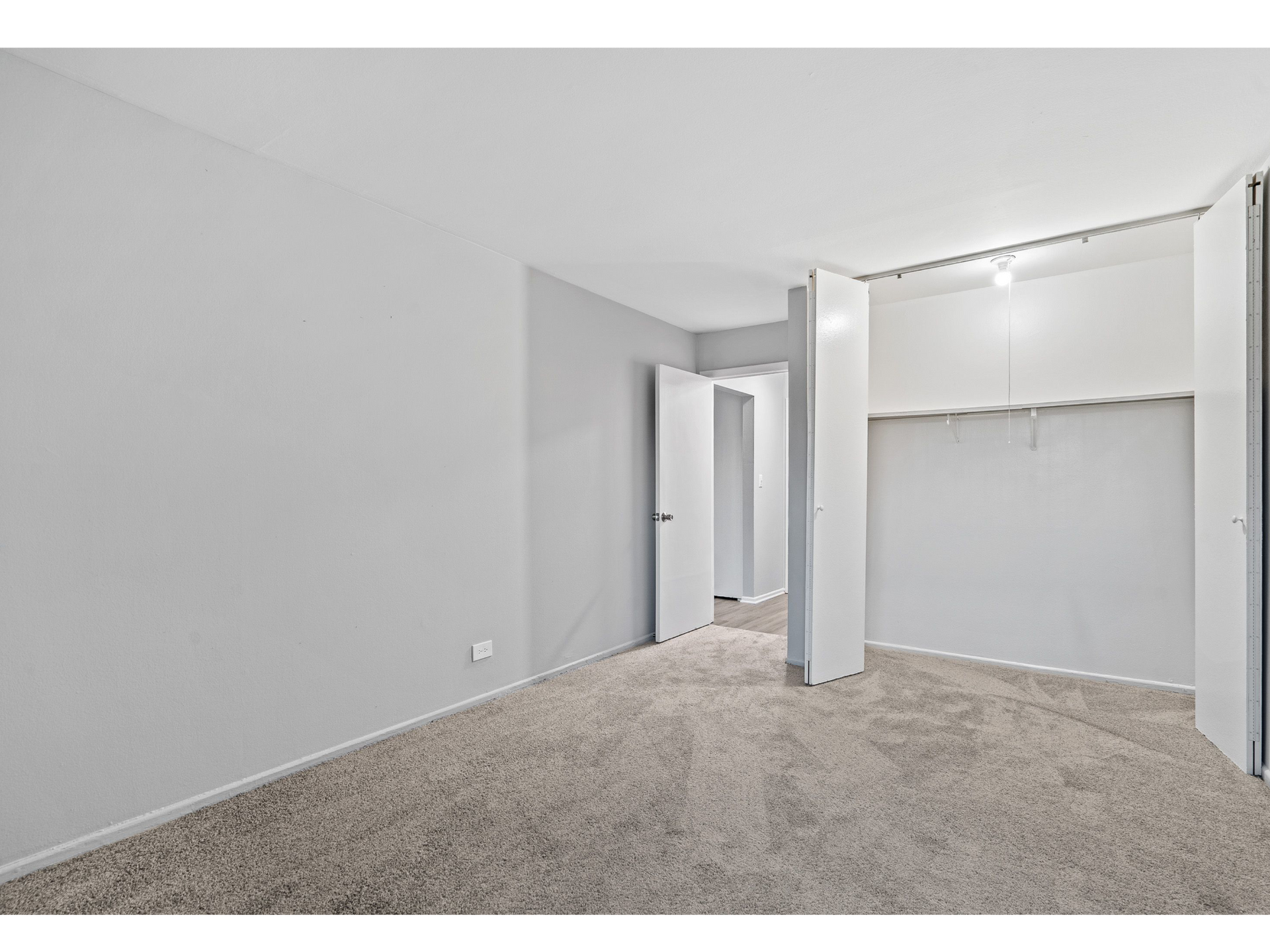 Empty bedroom with light gray walls, beige carpet, and open closet doors.
